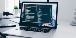 A MacBook with lines of code on its screen on a busy desk