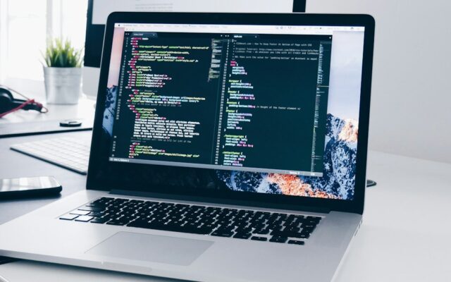 A MacBook with lines of code on its screen on a busy desk